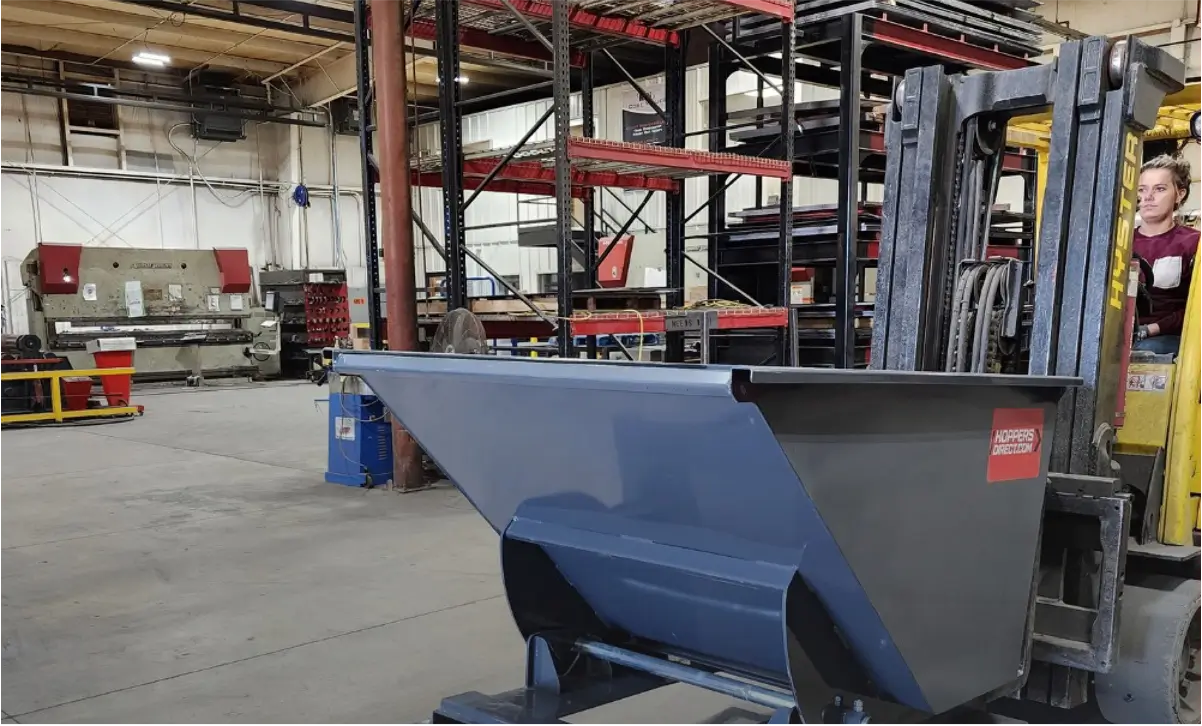 A Hoppers Direct forklift trash hopper is transported in a warehouse by a forklift.